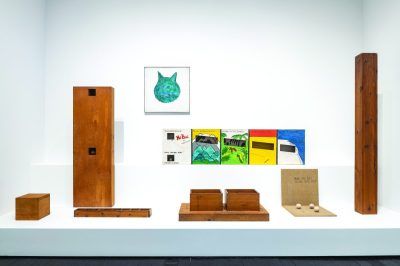 A group of variously sized boxy artworks arranged on a plinth with some more art installed on the wall behind.