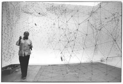 Black and white image of a woman in a gallery handling mesh forms that fill the space.