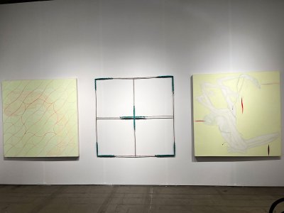 Two paintings done in the same pale green hang on either side of sculpture that resembles an empty canvas stretcher.