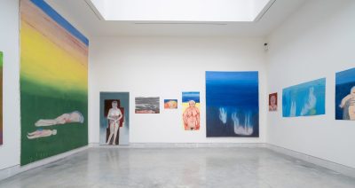 A skylit gallery space with colorful, variously sized figurative paintings lining the walls.