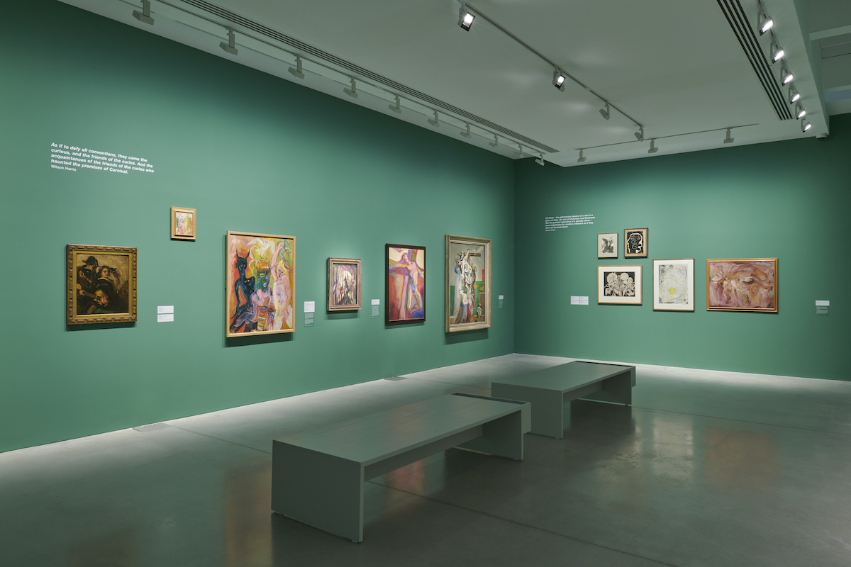A view of a gallery with green walls covered by 11 paintings of old and new vintage.