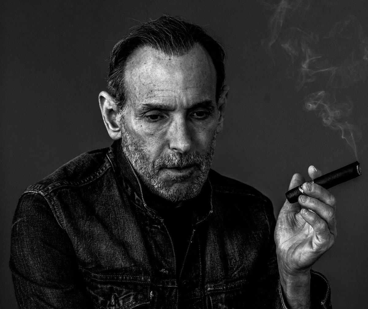 Black-and-white portrait of David Salle, an older white man who holds a lit cigar.