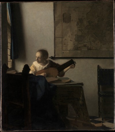 A young white woman looks out a window as she tunes a lute while sitting at a table. The room is mostly bathed in darkness, although a chair is visible in the background. A large map hangs on a wall.
