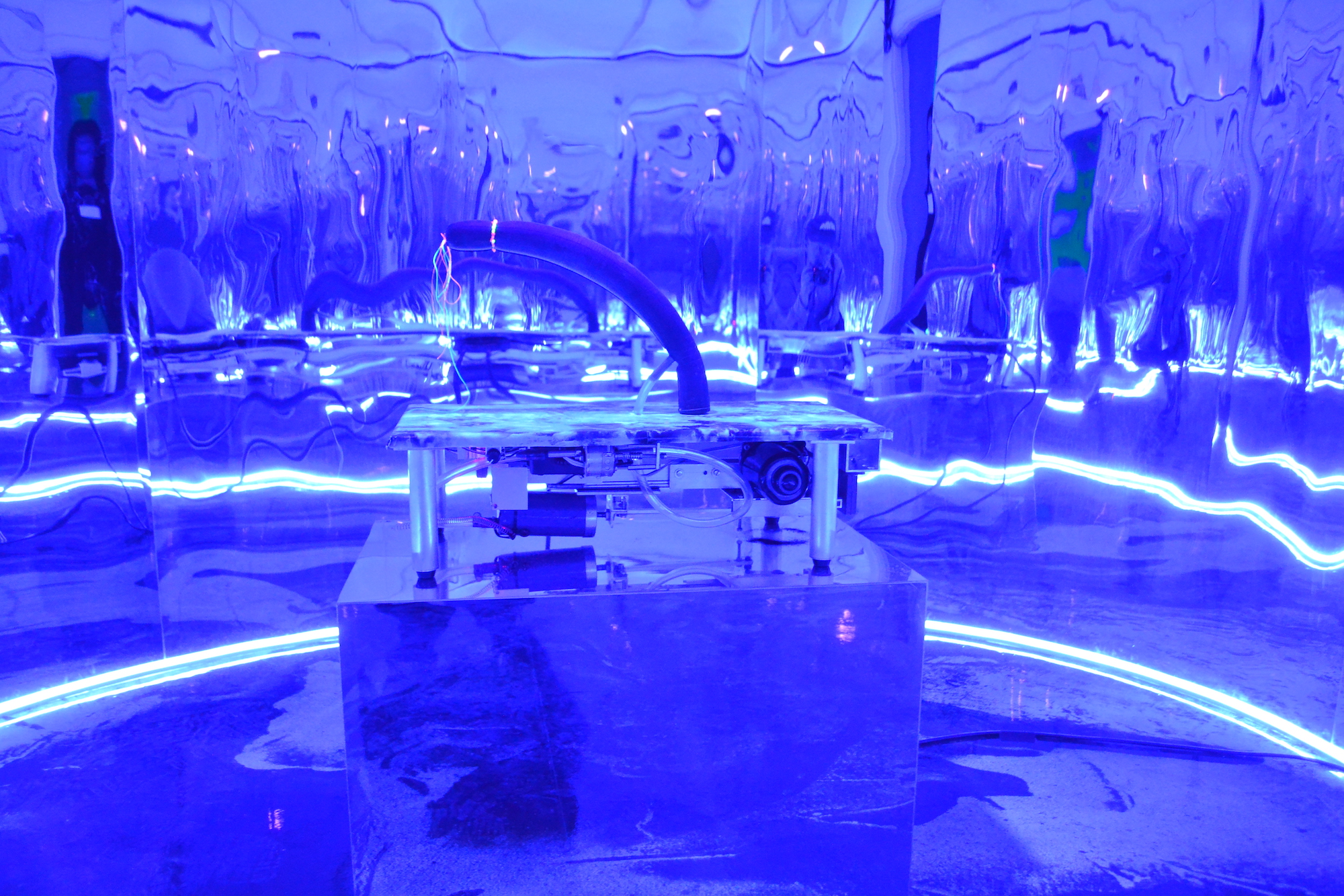 A mirror room illuminated by blue light and filled with metal contraptions.