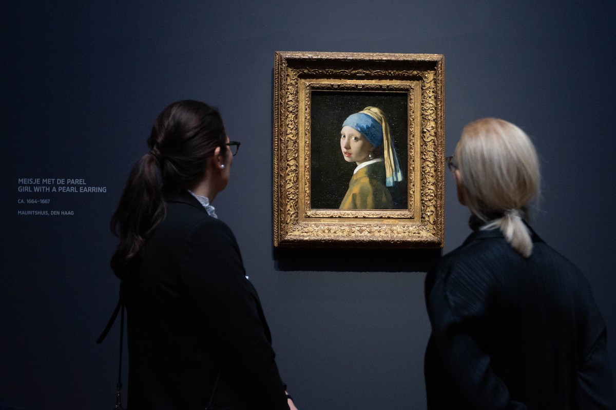 Two women looking at a painting of a woman wearing a turban staring out at the viewer.