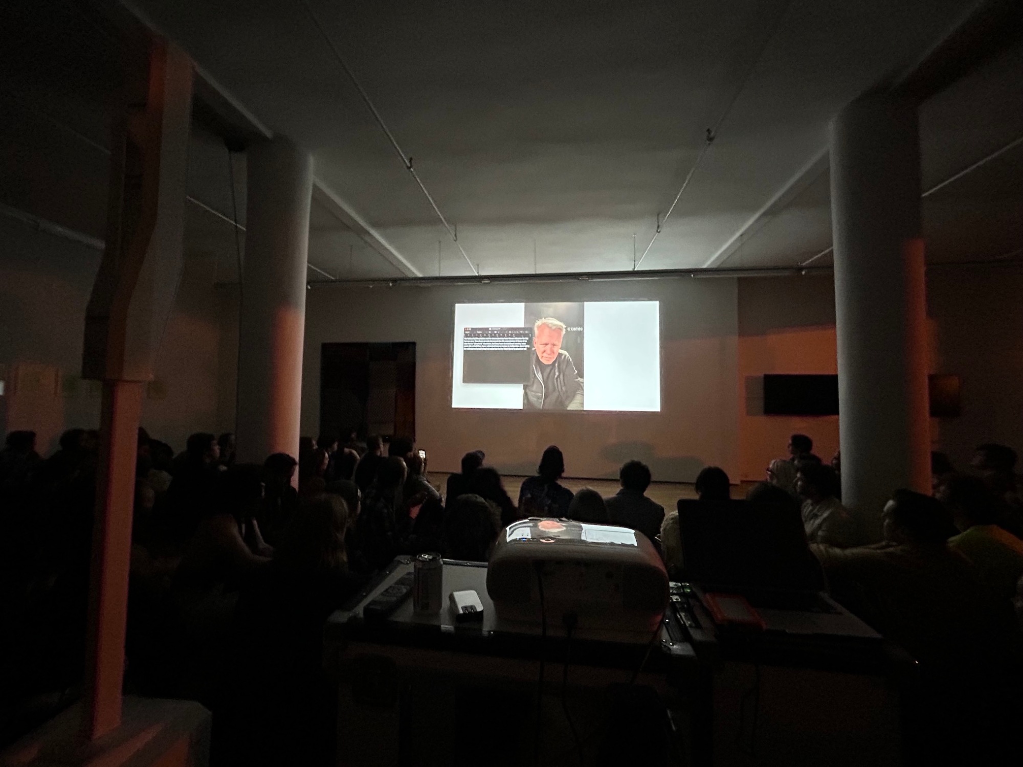 People sit in a dark room looking at a video projected on the wall.