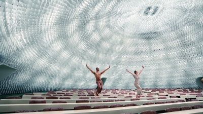 Two dancers atop rows of long white tables under a translucent domed ceiling.