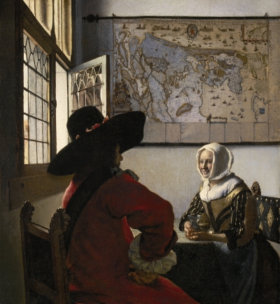 A white woman seated at a table with a glass laughs at a man in red seated with his back to us. He wears a large black hat. On the wall behind them is a map. A window is opened to allow light in.