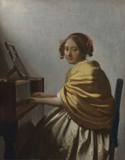 A young white woman sitting at a piano-like instrument in a chair. She wears a cream-colored shawl over her white dress and has red bows in her hair. She looks down toward the floor as her hands stroke the keys. Light pours in from an unseen window.