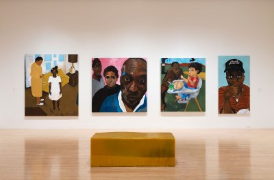 Four paintings by Henry Taylor hang on a museum wall in front of a yellow bench.