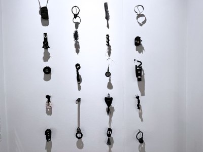 Several small-scale sculptures that are primarily all black made of various everyday items like plugs, combs, hair. Some include white cowrie shells.