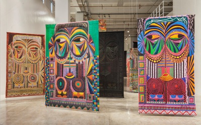 installation shot showing several colorful, ornate quiltlike works with abstracted figures