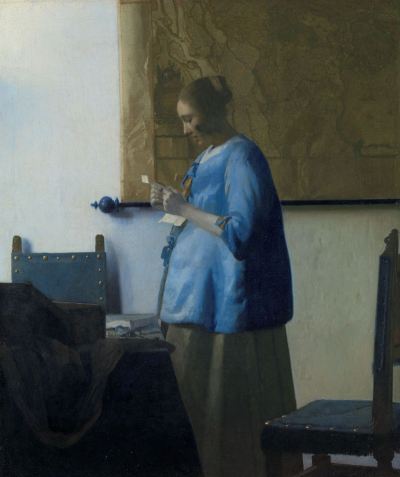 A white woman in a blue jacket and a green dress reading a letter that she holds in her two hands. She has stood up from a table, knocking a chair outward. Behind her is a large map.