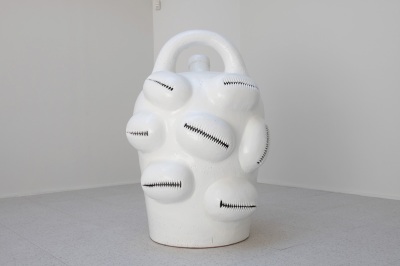 a large-scale white ceramic jug with a curved handle on top covered with forms resembling cowrie shells