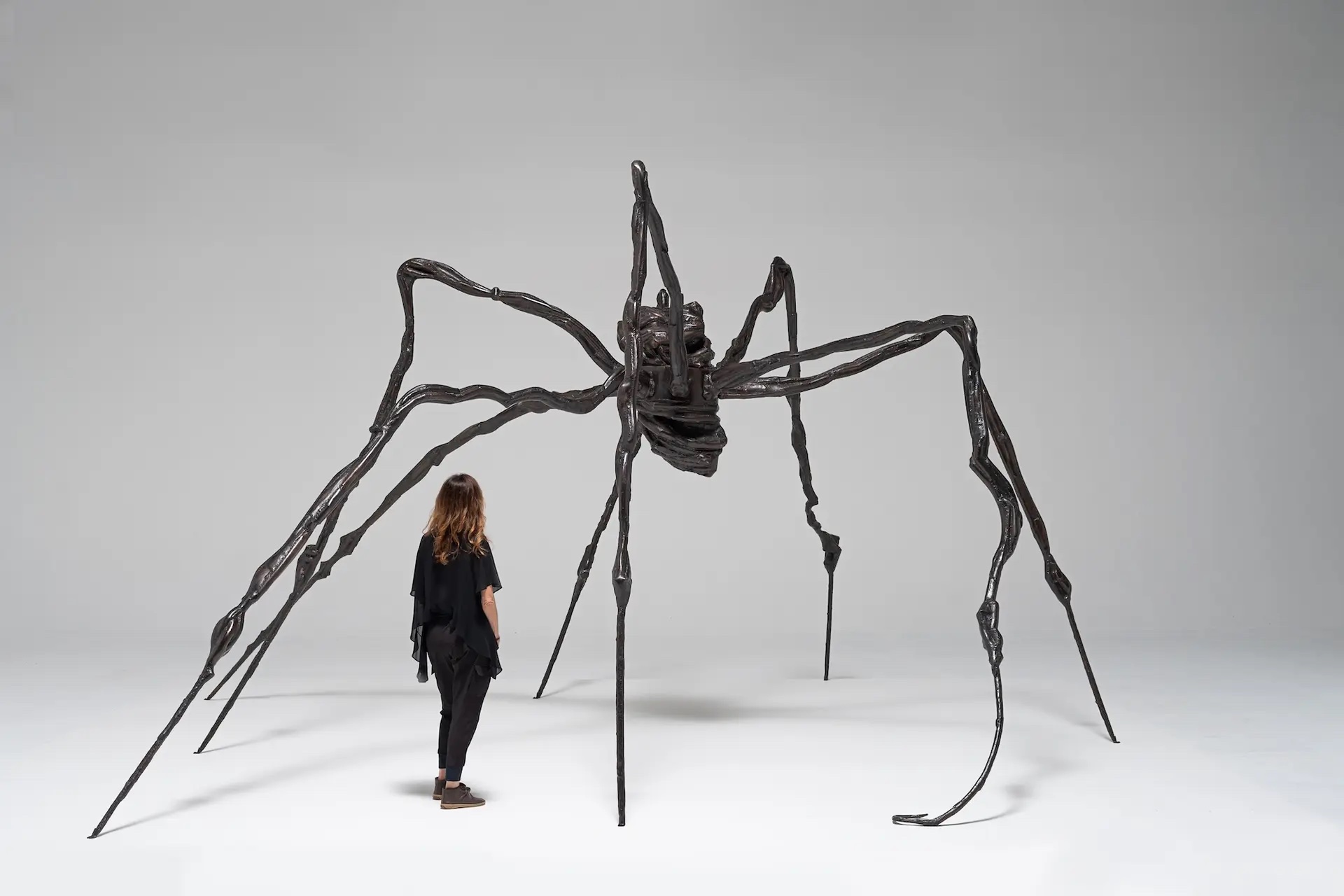 A woman standing beneath a large sculpture of a spindly spider.