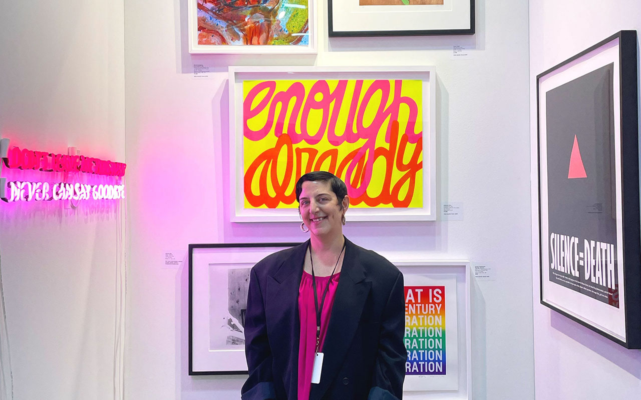 Portrait of Esther McGowan in front of various artworks including a Silence=Death poster.
