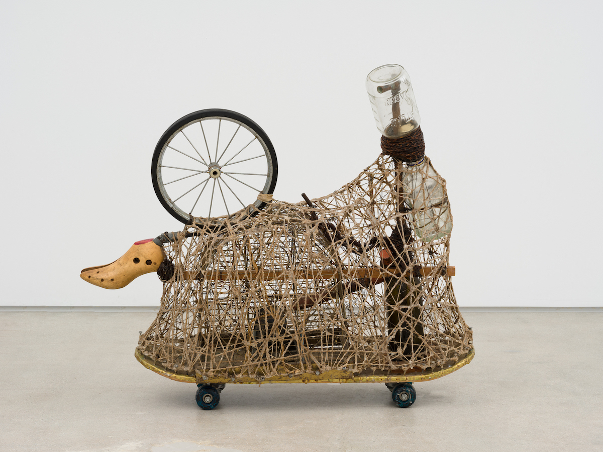 A twine wrapped assemblage of found objects propped on a skateboard.