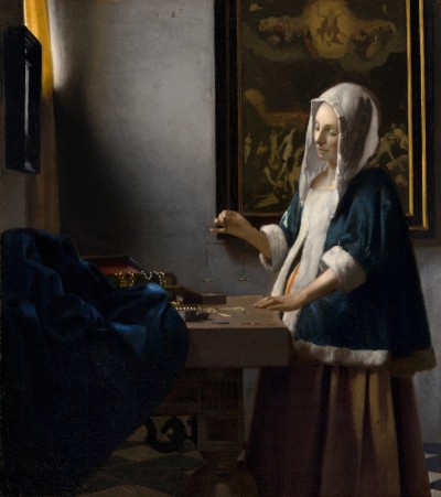 A white woman wearing a hood holding a balance before her at a table. Her belly bulges out beneath her blue jacket. The table is lined with jewels that catch light pouring in from a window above. Behind the woman is a painting of the Last Judgement, positioned so that Jesus rises up above the woman.