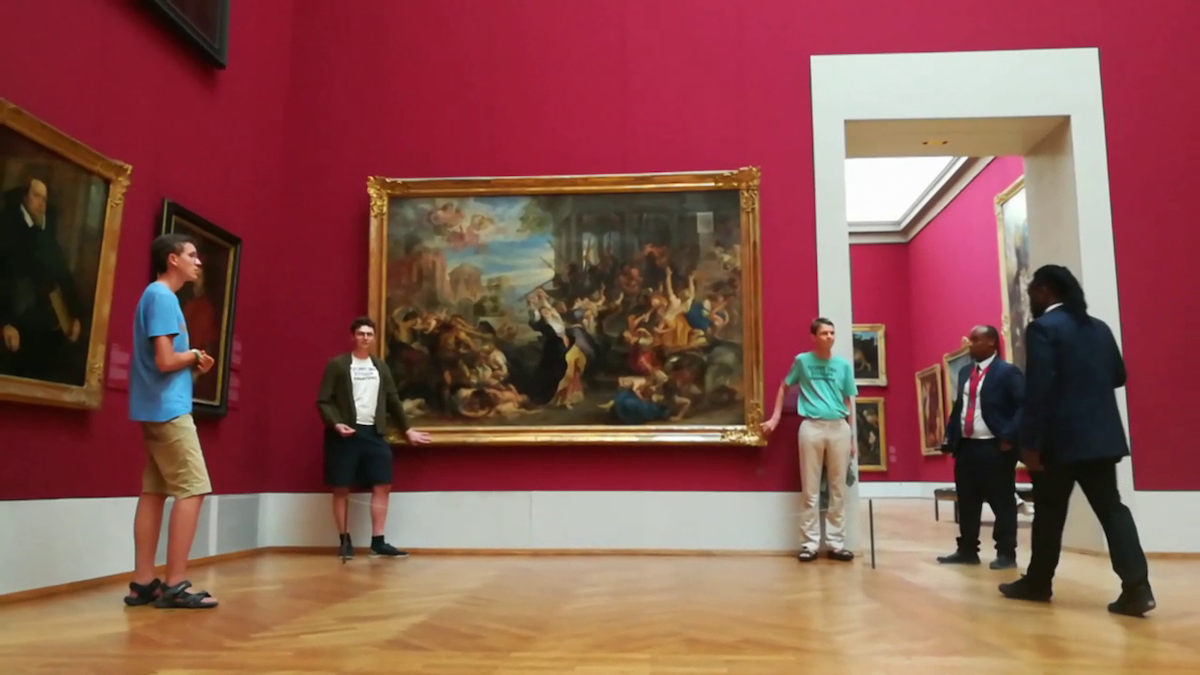 Two people with their hands attached to the frame of a painting in a red-walled gallery.